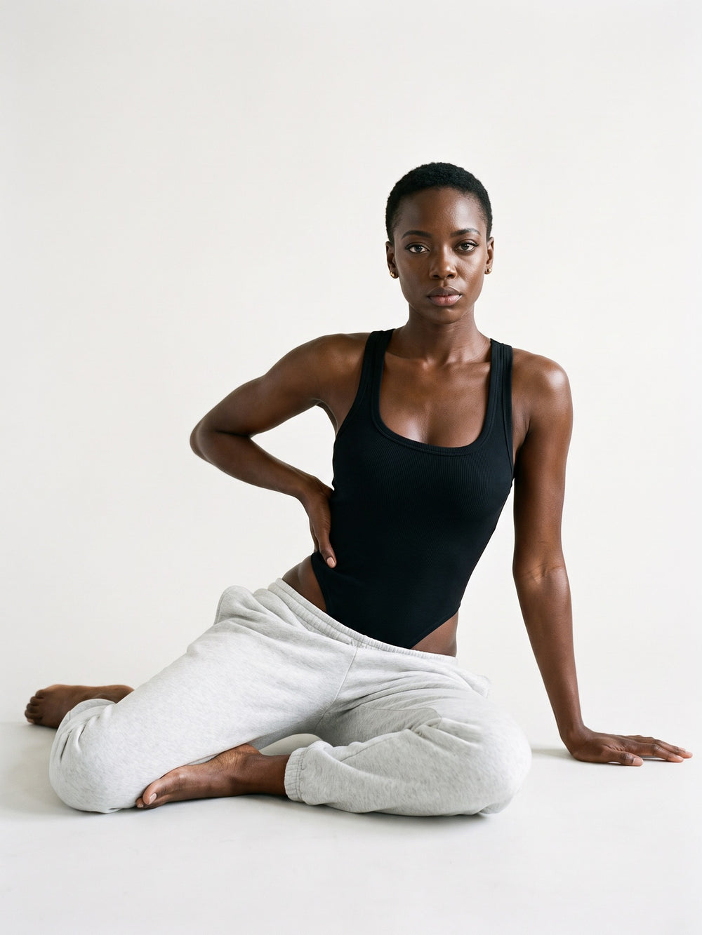 NOIR · Muse Sculpt Bodysuit noir, assise au sol jambes repliées